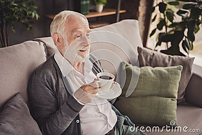 Photo of funny pensioner wear grey cardigan sitting couch having rest drinking coffee indoors house flat Stock Photo