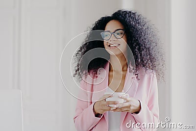 Photo of good looking African American prosperous busineswoman waits for partner in office, drinks coffee discusses future plans Stock Photo