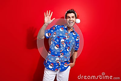 Photo of good mood friendly guy wear christmas hat print shirt waving hand to you say hello isolated on vivid red color Stock Photo