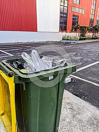 a photo of a green trash can full of plastic waste in an industrial area Stock Photo