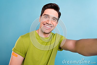 Photo of handsome funny young guy dressed green t-shirt smiling arm sticky plaster tacking selfie isolated blue color Stock Photo