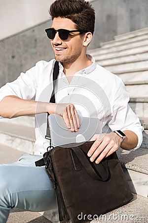 Photo of handsome man 30s wearing sunglasses, putting laptop int Stock Photo