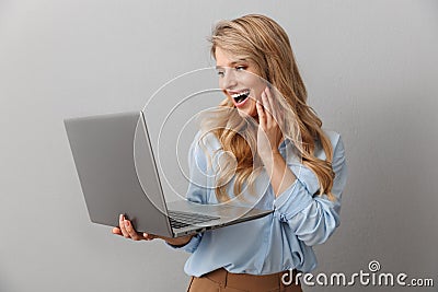 Photo of happy blonde woman 20s dressed in shirt smiling while holding and typing on silver laptop Stock Photo