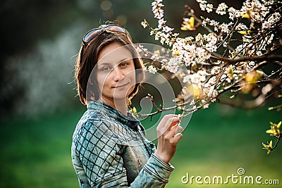Photo of happy middle-aged woman in blue jacket standing near branch of blooming tree Stock Photo