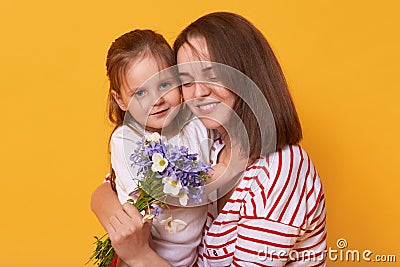 Photo of happy mother and kid. Affectionate female holds on tight her little charming daughter. Cute child gives bouguet of Stock Photo