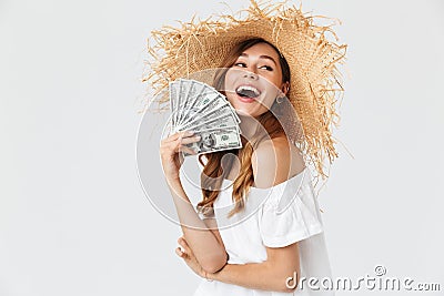 Photo of happy rich woman 20s wearing big straw hat rejoicing while demonstrating fan of dollar cash, isolated over white Stock Photo