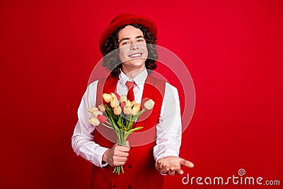 Photo of happy teenage boyfriend wearing formal suit gives you a hand invitation event and bunch tulips isolated on red Stock Photo