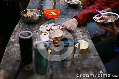 Photo of hiker`s breakfast wooden table with bread, bacon , cans, other meals and hot mugs at the forest camp. People Stock Photo