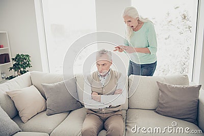 Photo of irritated aged man sitting on divan and listening to reproaches from scandalous aggressive lady counting his Stock Photo