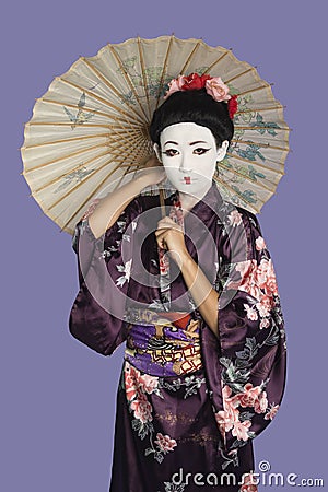 Portrait of Japanese woman in kimono with painted face holding parasol against purple background Stock Photo