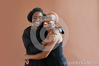 Photo of joyful dark skinned women dressed casually, smile positively, stand against brown background Stock Photo
