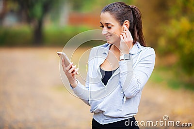 Photo of Joyful Fitness Woman 30s in Sportswear Touching Bluetooth Earpod and Holding Mobile Phone, While Resting in Stock Photo