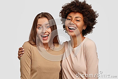 Photo of joyful ladies embrace and enjoy togetherness, being of different of races, dressed in casual jumpers, isolated Stock Photo