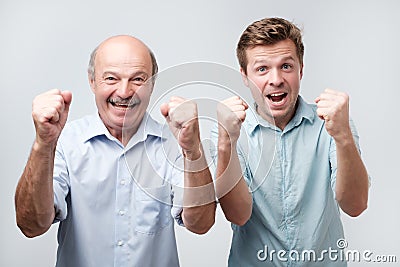 joyful two young men clench fists and shout with happiness, dressed casually, isolated on white background. Happy son and Stock Photo