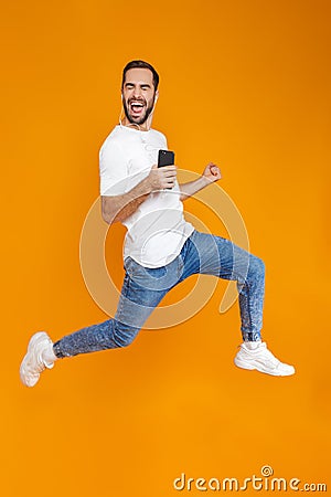 Photo of joyous man 30s singing while using earphones and mobile phone, isolated over yellow background Stock Photo