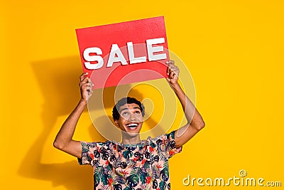 Photo of looking above head young promoter man in trendy t shirt holding red poster sale word isolated on yellow color Stock Photo