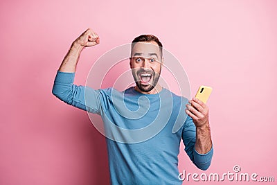 Photo of lucky young guy wear blue pullover holding modern gadget rising fist isolated pink color background Stock Photo