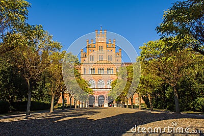Photo of main building of University from entrance gate on blue autumn sky and yellow and green foliage on trees. Architecture of Editorial Stock Photo