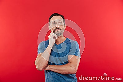Photo of man 30s wih brooding gaze in casual t-shirt looking upward and thinking or remembering, isolated over red background Stock Photo