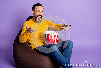 Photo of man sit beanbag hold remote control box popcorn wear yellow sweater jeans isolated purple background Stock Photo