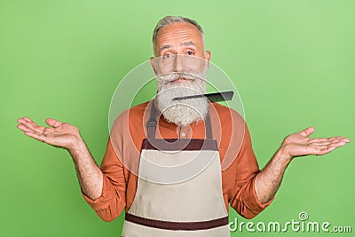 Photo of mature man hairdresser brush stack in beard clueless puzzled isolated over green color background Stock Photo