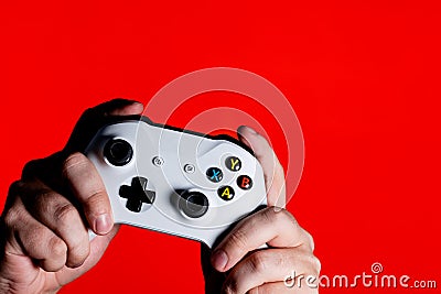 A photo of men hands holding a white gamepad on a bright red background with a place for the advertised text Stock Photo