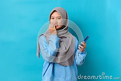 Photo of nervous scared Indonesian woman holding a smartphone with worried expression at camera, sees phobia, afraids of speaking Stock Photo