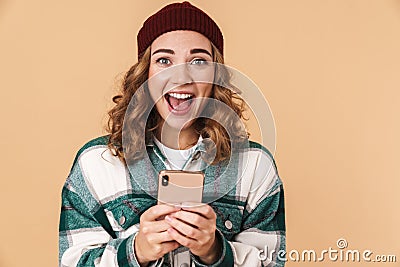 Photo of nice excited woman in knit hat smiling and using cellphone Stock Photo