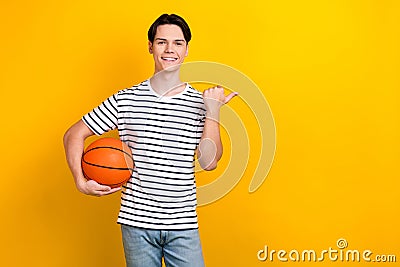 Photo of nice student dressed striped t-shirt hold bascketball ball indicating at offer empty space isolated on yellow Stock Photo