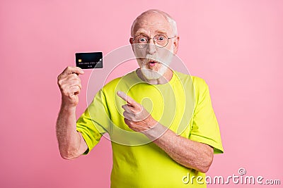 Photo of old shocked amazed surprised grandfather wear lime t-shirt point finger credit card isolated on pink color Stock Photo