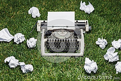 Photo of old typewriter on a green grass with a sheet of paper. Stock Photo