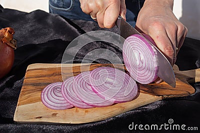 Photo of the onion slicing process. A woman cuts onions into circles with a knife Stock Photo