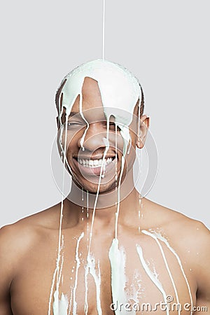 Paint falling on shirtless young Hispanic man`s head against gray background Stock Photo