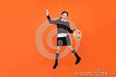 Photo of painter cute schoolgirl jump hold palette brush wear uniform isolated orange color background Stock Photo