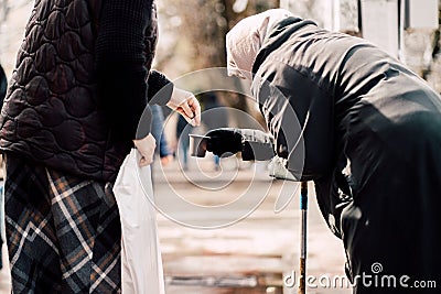 Photo of passerby givining alms for old hungry homeless female beggar on street Editorial Stock Photo