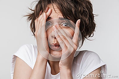 Photo of perplexed woman with short brown hair in basic t-shirt keeping hand over her face and looking at camera Stock Photo