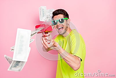 Photo portrait crazy man wearing bright t-shirt shooting with banknotes from gun isolated pastel pink color background Stock Photo