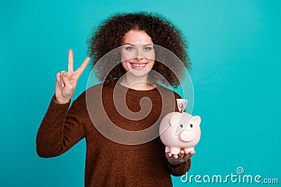 Photo portrait of pretty young girl piggy money account show v-sign dressed stylish brown outfit isolated on aquamarine Stock Photo