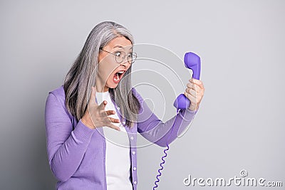 Photo portrait of senior mad furious stressed woman shouting screaming loudly keeping handset of retro violet phone with Stock Photo