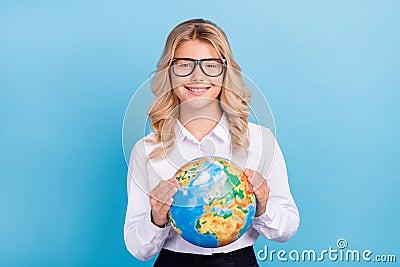 Photo of positive schoolgirl hold globe toothy beaming smile wear specs shirt isolated blue color background Stock Photo