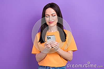 Photo of positive woman with straight hairdo dressed orange t-shirt read message on smartphone isolated on purple color Stock Photo