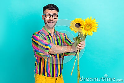 Photo of positive young person toothy smile hands hold bunch sunflowers give empty space isolated on cyan color Stock Photo