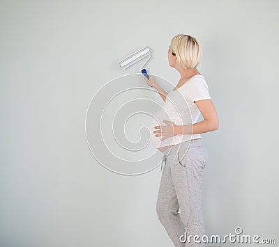 Photo of a pregnant female painting the wall of a bedroom for her future baby. Stock Photo