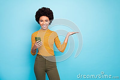 Photo of pretty dark skin wavy lady hold telephone open palm presenting novelty smartphone product wear yellow striped Stock Photo