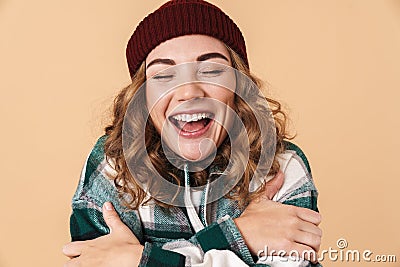 Photo of pretty excited woman in knit hat hugging herself and laughing Stock Photo