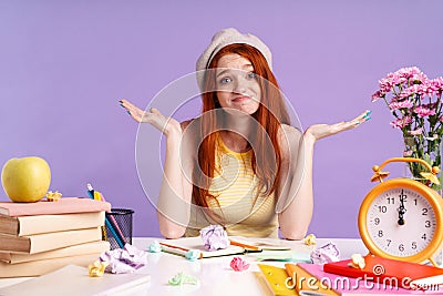 Photo of puzzled student girl throwing up hands sitting at desk with books Stock Photo