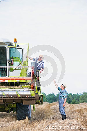 Senior farmer talking to mature farmer standing on harvester in field Stock Photo