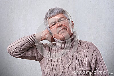 A photo of senior man wearing glasses being tired from hard work holding his hand on head. A mature man having headache after work Stock Photo