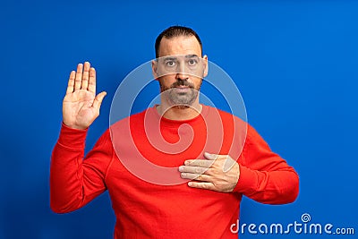 Photo of serious and confident bearded hispanic man with hand on chest promising oath isolated over blue colored Stock Photo