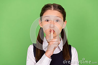 Photo of serious pretty schoolgirl wear formal outfit finger lips asking keep silence green color background Stock Photo
